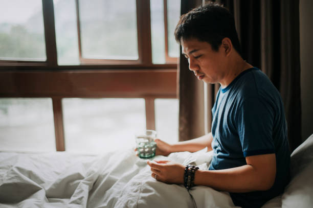 집에서 아시아 중국 여성 아픈 질병과 온도계를 사용하여 자신의 체온을 확인하고 침대에 물과 약을 복용 - pill men home interior one person 뉴스 사진 이미지