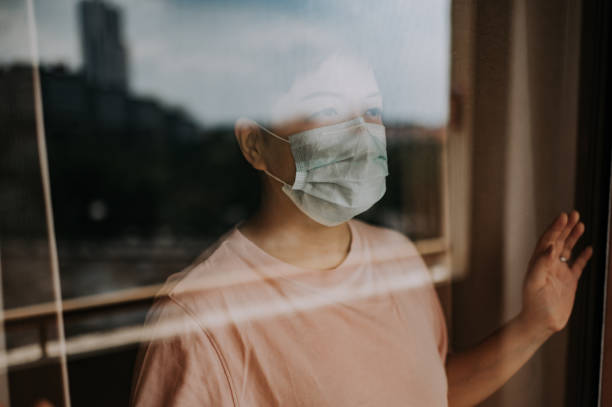 une femelle chinoise asiatique regardant à travers sa fenêtre de balcon avec son masque facial pendant l’ordre restreint de mouvement en malaisie - solitary confinement photos et images de collection