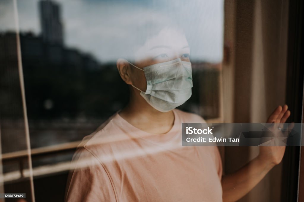 an asian chinese female looking thru her balcony window with her face mask during the restricted movement order in malaysia an asian chinese female looking out from her balcony window with her face mask during the restricted movement order in malaysia Coronavirus Stock Photo