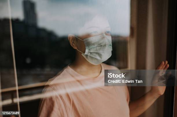 An Asian Chinese Female Looking Thru Her Balcony Window With Her Face Mask During The Restricted Movement Order In Malaysia Stock Photo - Download Image Now