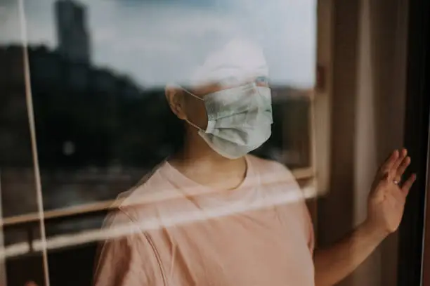 an asian chinese female looking out from her balcony window with her face mask during the restricted movement order in malaysia