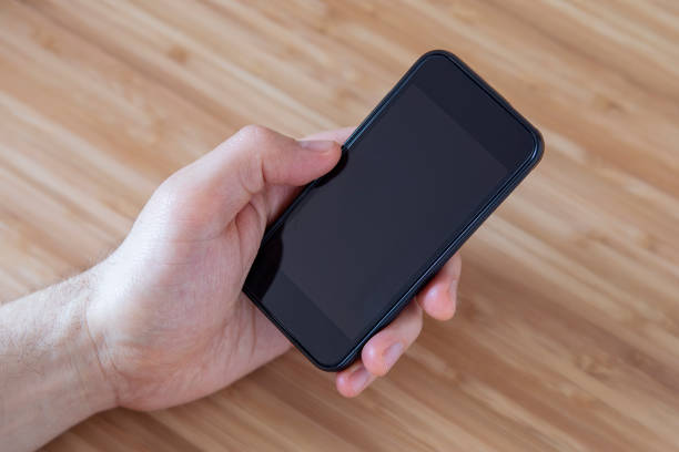 istock Man holding blank smartphone with his left hand, blank display close up, neutral background, view from above. Communication concept. 1215679884