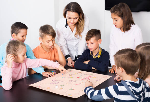 istock Teacher and happy kids sitting  at table with board game 1215680757