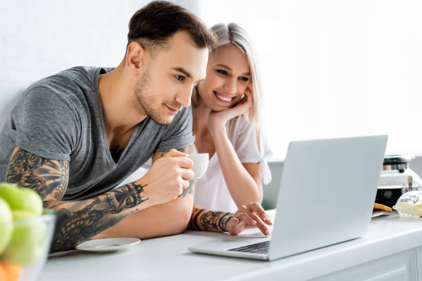 istock Selective focus of smiling tattooed couple using laptop during breakfast in kitchen 1215681919
