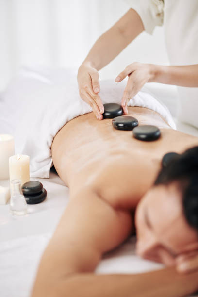 Latone therapy Massage therapist putting warm massage stones along spine of spa salon client hot stone massage stock pictures, royalty-free photos & images