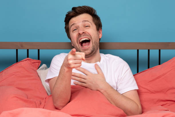 istock Laughing satisfied man pointing at you sitting on the bed 1215685301
