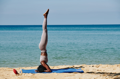 Fit slim young woman doing headstand on sandy beach in the morning