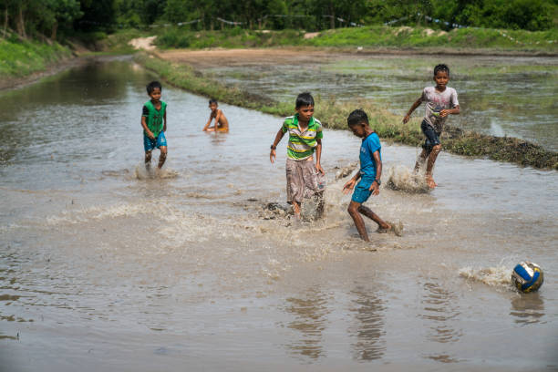 차우 닥, 베트남 - 2018년 10월 13일: 축구공을 들고 진흙 투성이의 물밭에서 노는 베트남 어린이들 - child mud dirty football 뉴스 사진 이미지