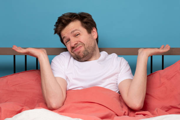 istock Confused caucasian man is unsure in bed shrugging hands. 1215688158