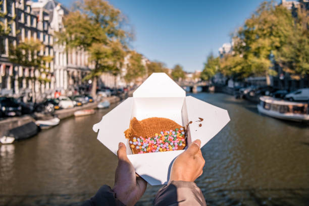 amsterdam nederland, vrouwenhand met stroopwafel in amsterdam - typisch nederlands eten - twee ronde stukken wafel gevuld met karamelachtige siroop - stroopwafel stockfoto's en -beelden