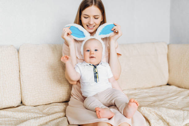 istock Happy Easter. A mother and a small baby, with rabbit ears on Easter day, have fun, play and cuddle while sitting on the sofa 1215693435
