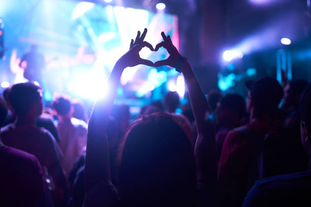 Crowd of Audience at during a concert with silhouette of a heart shaped hands shadow. stock photo