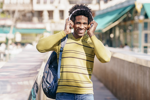 Black man with afro hair listening to music with wireless headphones sightseeing in Granada, Andalusia, Spain.