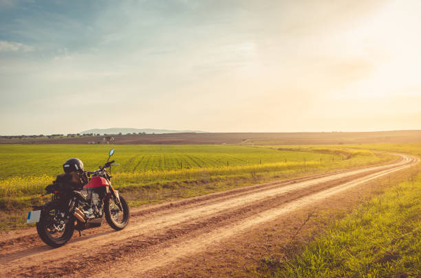Male motorcycle adventure rider seen on a dirt road in beautiful nature with grass and flower fields around him during one sunny day.