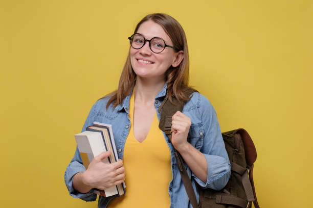 istock Young happy woman with backpack and glasses holding several books 1215700822