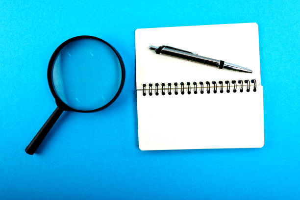 istock Magnifying glass with empty blank and pen on blue table. 1215701067