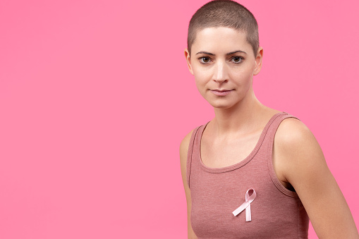 Waist up portrait of a young woman wearing pink breast cancer awareness ribbon isolated over pastel pink background. Healthcare, people, charity and medicine concept.