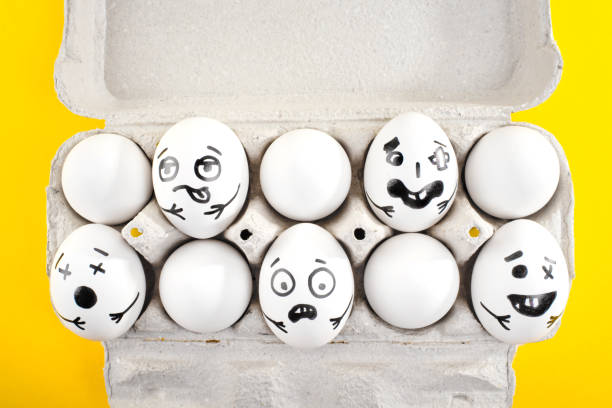 istock Easter eggs with drawn cartoon faces in a cardboard tray on yellow background. Close up. 1215704417