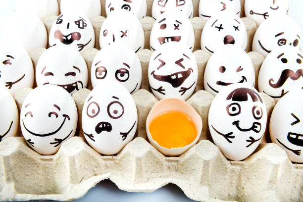 istock Eggs with drawn cartoon faces and one broken egg in tray.  Easter postcard. 1215705160