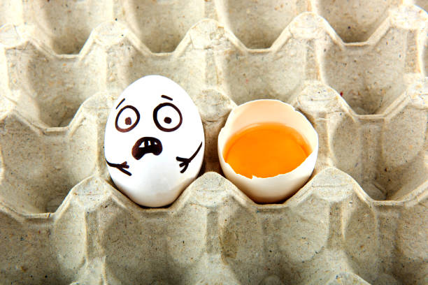 istock Egg with drawn cartoon faces and one broken egg in tray. 1215705253