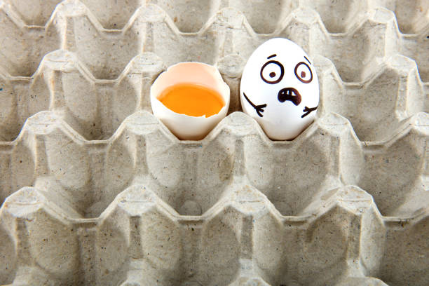 istock Egg with drawn cartoon faces and one broken egg in tray. 1215705266