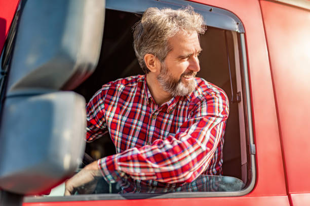Mature truck driver sitting in his truck and parking. Happy truck driver wearing casual clothing sitting in his truck and parking, looking over shoulder. truck photos stock pictures, royalty-free photos & images
