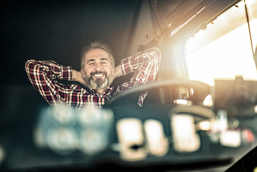 Happy truck driver wearing casual clothing sitting in his truck, chilling and smiling.