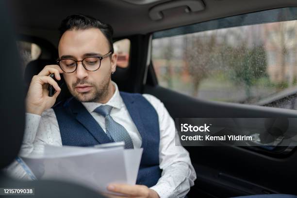 Confident Turkish Businessman Reading Document While Talking On Smart Phone In Car Stock Photo - Download Image Now