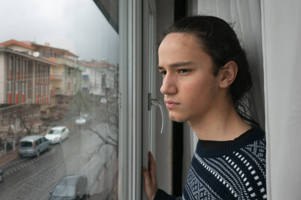 Young adult looking to empty street in anxiety from his home stock photo