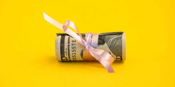 작은 달러 선물, 분홍색 리본으로 묶여 백 달러의 지폐의 번들. 노란색 배경에 고립 된 달러 - hundred dollars 뉴스 사진 이미지