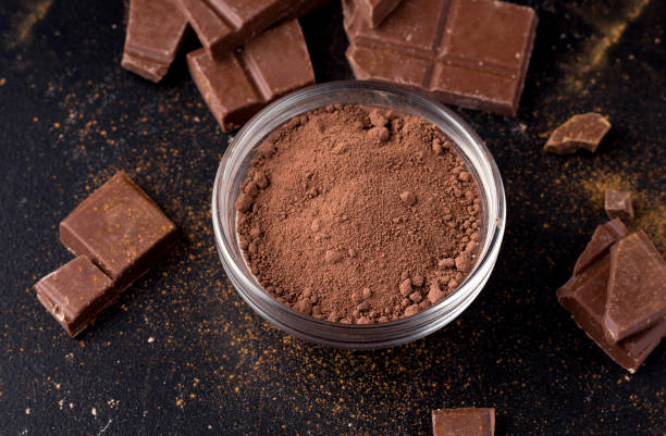 istock Cocoa powder in a plate on a black background next to chocolate. close-up 1215711549