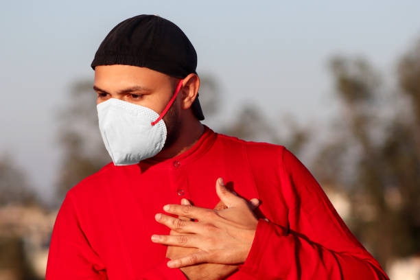 uomini con dolore toracico, che si coprono il viso con maschera antinquinamento per la protezione contro covid-19 - hand on heart immagine foto e immagini stock