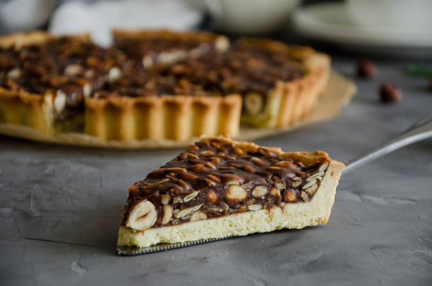 istock Tart with chocolate caramel, hazelnuts, peanuts, almonds and seed mix on a dark concrete background. Horizontal orientation. 1215713582