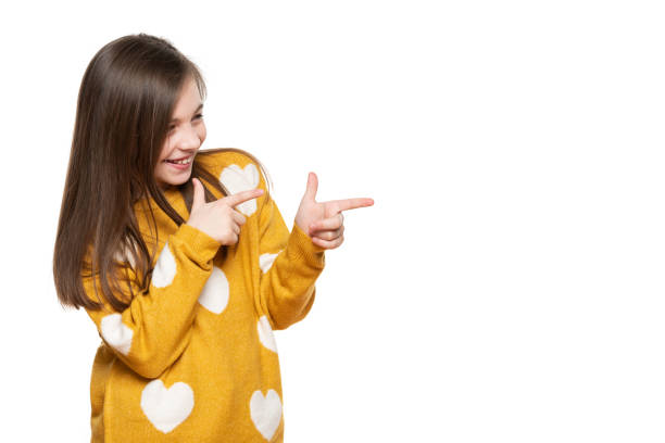 beautiful young girl in mustard yellow sweater llaughing while pointing to the side. waist up studio shot on white background. - carefree joy children only pre adolescent child imagens e fotografias de stock