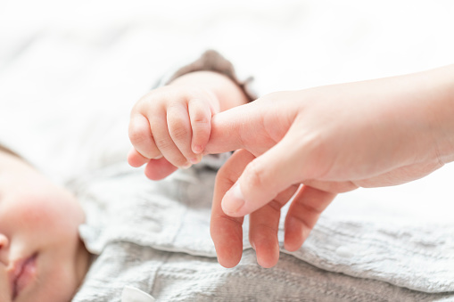 Mothers hand holding baby hand in bright room