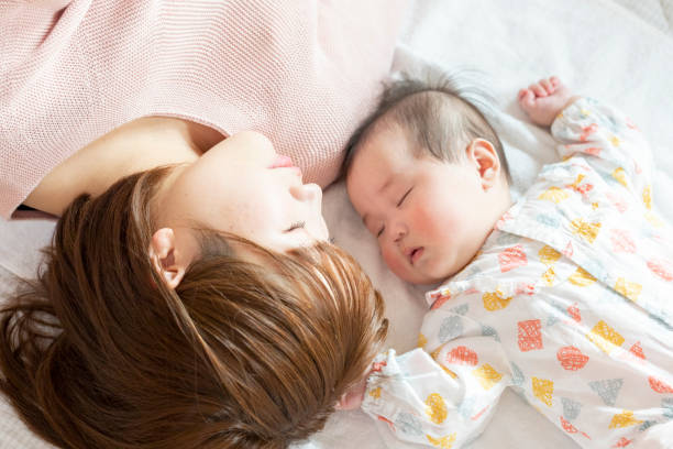 明るい部屋で赤ちゃんと一緒に寝ているママ - 家族　寝る ストックフォトと画像