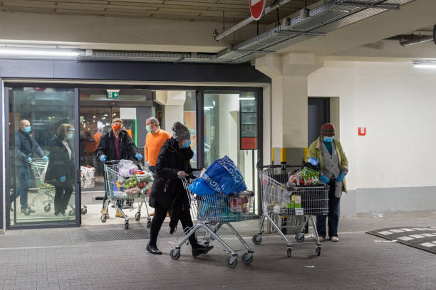 Ealdery people with protective medical masks and gloves leaving grocery shopping store with shopping carts full of groceries. Panic buying during coronavirus senior shopping hours. Coronavirus lockdown. stock photo