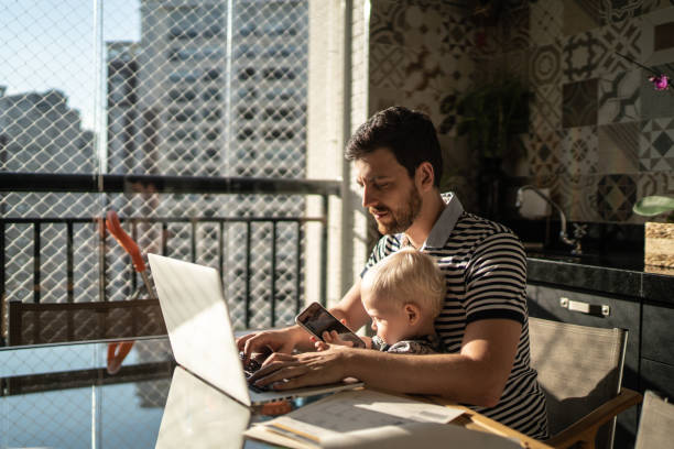 istock Man holding his son and working with laptop at home 1215724856