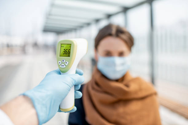 Measuring temperature of a young woman in face mask at a checkpoint outdoors Measuring temperature with infrared thermometer of a young woman in face mask at a checkpoint during an epidemic outdoors. Concept of prevention the spread of the virus covid thermometer stock pictures, royalty-free photos & images