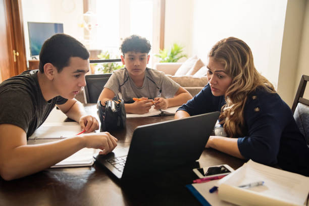 Mother homeschooling teenage boys in self-isolation, Covid-19. Mother homeschooling teenage boys from home on dinner table in small city apartment self-isolating from Covid-19. Mother and boys are latin american. Horizontal waist up indoors shot with copy space. homework stock pictures, royalty-free photos & images