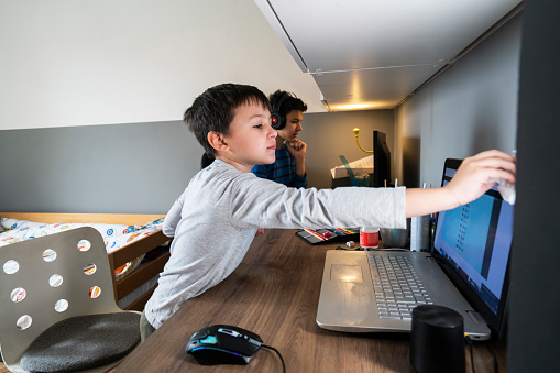 Boy wiping laptop and desk, while his brother is at home schooling