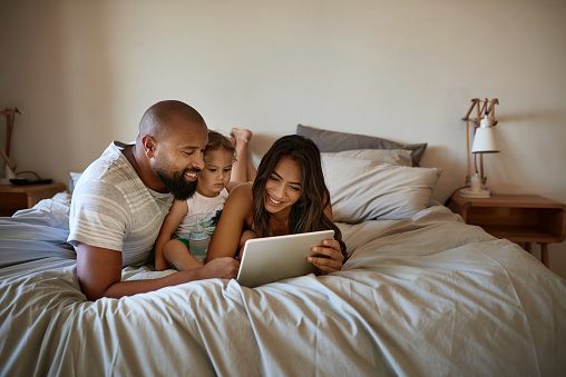 Shot of an affectionate young family of three using a tablet while relaxing on a bed at home