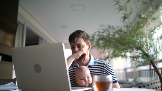Worried man holding son and working with laptop at home