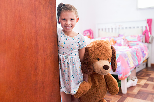 Portrait of an adorable little girl holding a teddybear and opening the door of her bedroom