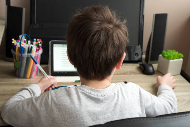 istock Boy studying at home with tablet and doing school homework. Distance learning online education or stay at home concept. Soft focus. Back view 1215732027