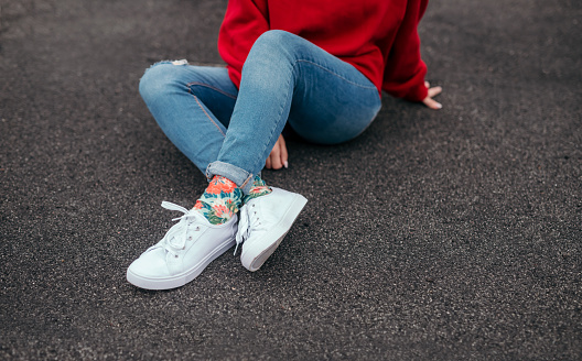 Unrecognizable young female in casual outfit and floral socks sitting on asphalt on city street