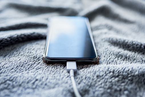 Closeup of a cellphone being charged on top of a bed inside during the day