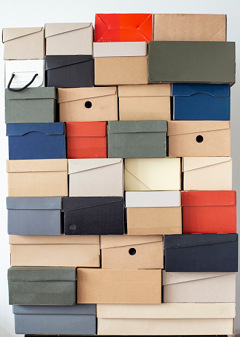Stack of unevenly folded shoe boxes against a white wall. Seasonal sales and discounts. Vertical photo.