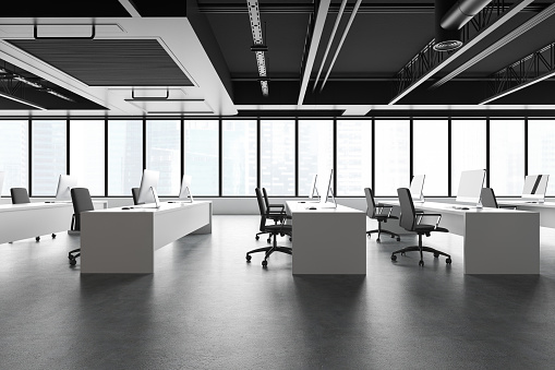 Side view of spacious industrial style open plan office with concrete floor, rows of long computer tables and panoramic window with cityscape. 3d rendering