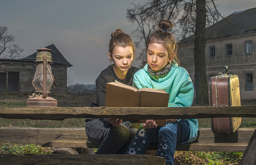 Girls read a book near the old manor on a wooden bench.